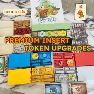 May include: An assortment of board game components, including tokens, cards, and storage trays. The game box, titled "Emberleaf," is visible, along with the text "Premium Insert Token Upgrades." Various colors are present, including red, blue, yellow, and beige.