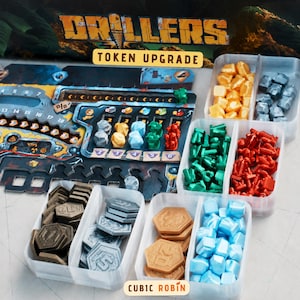 May include: A board game token upgrade set for Drillers, featuring various coloured plastic resource pieces and hexagonal tokens organised in clear divided trays. The game board displays numerical tracks, icons, and the text Drillers Token Upgrade.