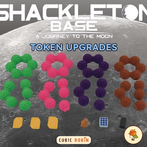 May include: An advertisement for "Shackleton Base: A Journey to the Moon" game, showcasing "Token Upgrades." The image displays colourful spherical game tokens in green, pink, purple, and orange, plus other game pieces.