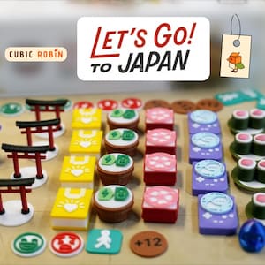 Może przedstawiać: Kolekcja miniaturowych elementów i żetonów do gier, w tym sushi, bramy torii i konsole do gier. Obraz zawiera tekst "Let's Go to Japan" i "Cubic Robin". Obecne są różne kolory, w tym czerwony, żółty, zielony i fioletowy.