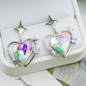 Pu&ograve; includere: Un paio di orecchini a forma di cuore color argento con centri di cristallo iridescenti multicolore. Ogni orecchino presenta un accento a forma di stella nella parte superiore e piccoli dettagli a stella attorno al cuore. Un piccolo cristallo trasparente &egrave; incastonato su ogni orecchino.