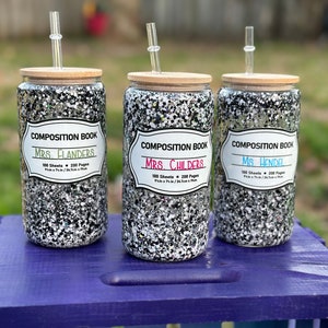 May include: Three black and white glitter tumblers with bamboo lids and clear straws. Each tumbler has a white label with the text "Composition Book" and a teacher's name: "Mrs. Flanders", "Mrs. Childers", and "Ms. Hendel".