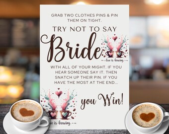 May include: A white card with brown text that reads "Grab two clothes pins & pin them on tight. Try not to say Bride --love is brewing-- With all of your might. If you hear someone say it. Then snatch up their pin. If you have the most at the end... you Win!" The card has a watercolor illustration of two coffee cups with hearts and coffee beans.