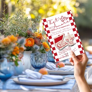 May include: Engagement party invitation with a red and white checkered border. The invitation features the words "That's Amore" in cursive, along with illustrations of pizza and wine. The invitation also includes the date, time, and location of the event.