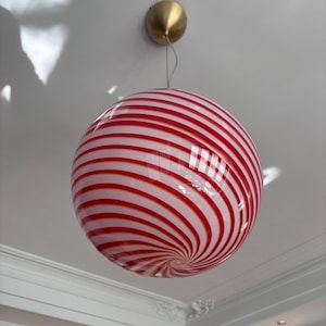 May include: A spherical pendant light fixture with a red and white striped pattern. The light hangs from a brass-colored ceiling mount. The glass globe has a spiral design.
