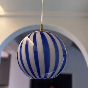 Puede incluir: Una lámpara colgante de globo con rayas blancas y azules y una parte superior de metal dorado.
