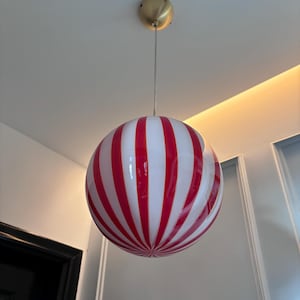 May include: A red and white striped glass globe pendant light fixture hanging from a ceiling.