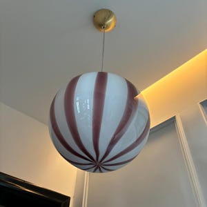 Può includere: Un lampadario a globo in vetro a strisce bianche e rosa con un supporto a soffitto in metallo dorato.
