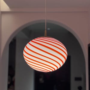 Könnte beinhalten: Eine rote und weiße gestreifte Glaspendelleuchte hängt von der Decke.