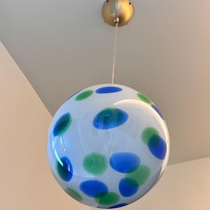 May include: A white, spherical pendant light fixture with blue and green polka dots. The light hangs from a gold-colored ceiling mount. The glass globe is a decorative lighting element.