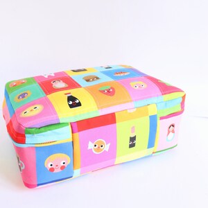 Puede incluir: Una bolsa rectangular con cremallera de colores con un dise&ntilde;o de patchwork que presenta varios personajes y objetos de dibujos animados. La bolsa est&aacute; hecha de tela y tiene un cierre de cremallera.