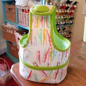 May include: A green and white fabric storage bin with a clothespin pattern. The bin has a green handle and a green lining.