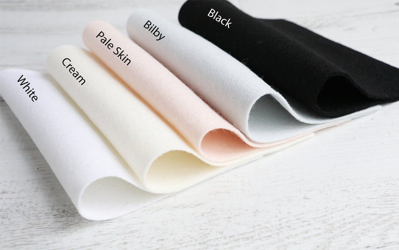 Puede incluir: Cinco muestras de tela de fieltro en diferentes colores: blanco, crema, piel p&aacute;lida, bilby y negro. Las muestras est&aacute;n dobladas y dispuestas en una fila de la m&aacute;s clara a la m&aacute;s oscura.