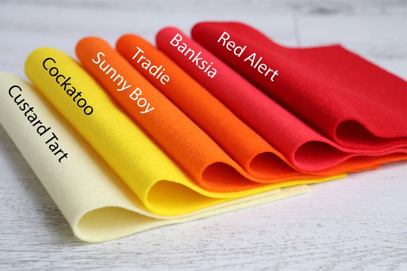 Puede incluir: Cinco muestras de tela de fieltro de diferentes colores, dispuestas en degradado de amarillo claro a rojo. Las muestras est&aacute;n etiquetadas con los nombres "Custard Tart", "Cockatoo", "Sunny Boy", "Tradie", "Banksia" y "Red Alert".