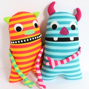May include: Two striped plush toys with friendly faces. One is orange and yellow with green and pink arms. The other is blue and white with pink arms.