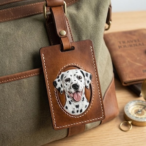 Può includere: Un'etichetta per bagagli in pelle marrone con un ritratto di cane dalmata. L'etichetta è attaccata a una borsa da viaggio in tela verde con dettagli in pelle marrone. Un diario di viaggio e una bussola sono sullo sfondo.