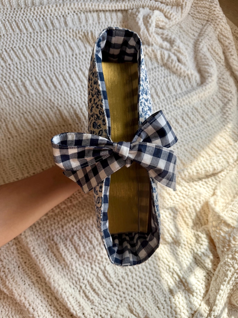K&ouml;nnte beinhalten: Ein handgefertigter Schuh mit blauem Blumenmuster und einer Vichy-Schleife. Die Innenseite ist goldfarben. Der Schuh wird vor einem cremefarbenen, strukturierten Hintergrund pr&auml;sentiert.