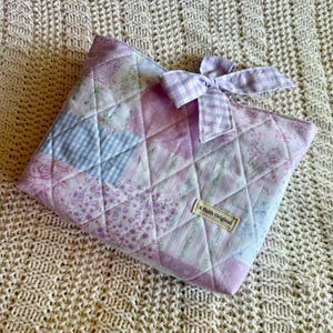 K&ouml;nnte beinhalten: Gesteppte Patchwork-Tasche in Lavendel-, Rosa- und Blaut&ouml;nen mit einer Vichy-Schleife. Die Tasche hat ein Rautenmuster und ein Etikett mit der Aufschrift "A Faith Original".