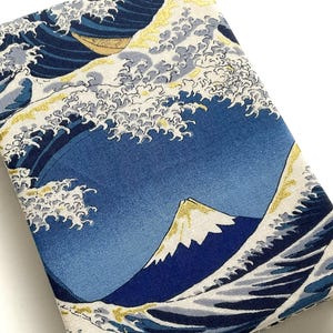Könnte beinhalten: Ein rechteckiger Stoffartikel mit einem japanischen Wellenmuster und einem Berg im Hintergrund. Das Design verwendet Blau-, Weiß- und Goldtöne. Der Artikel ist wahrscheinlich eine Hülle oder ein Bezug.