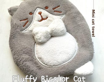 May include: A gray and white fluffy cat-shaped hand towel with a bow tie. The towel is labeled "Mini cat towel" and "Fluffy Bicolor Cat".