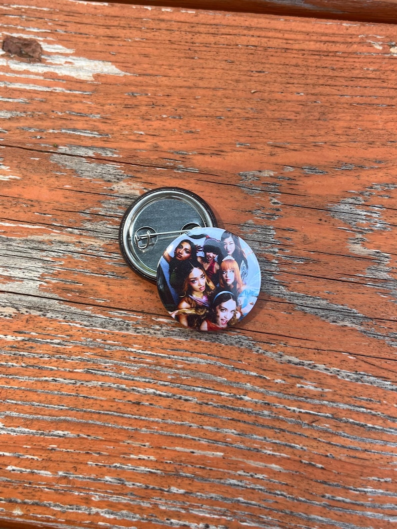 May include: A circular pin-back button featuring a colorful photographic collage of five individuals with diverse hairstyles and expressions. The button has a metallic silver backing with a pin mechanism visible, showcasing the construction of the accessory.