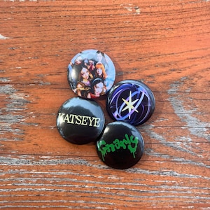 May include: Four round pinback buttons with various designs. One button features a group of women, another has a starburst design, and a third says "KATSEYE". The last button has the word "Gnarly" in green.