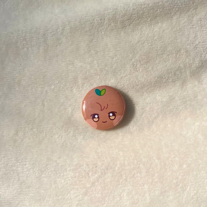 Puede incluir: Un bot&oacute;n marr&oacute;n con una cara de dibujos animados y hojas verdes en la parte superior. La cara tiene dos ojos grandes, una boca peque&ntilde;a y una sola l&iacute;nea para la nariz.