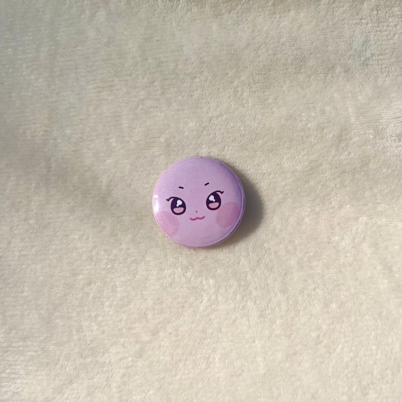 Puede incluir: Un bot&oacute;n morado con una cara de dibujos animados con ojos grandes y mejillas sonrosadas.