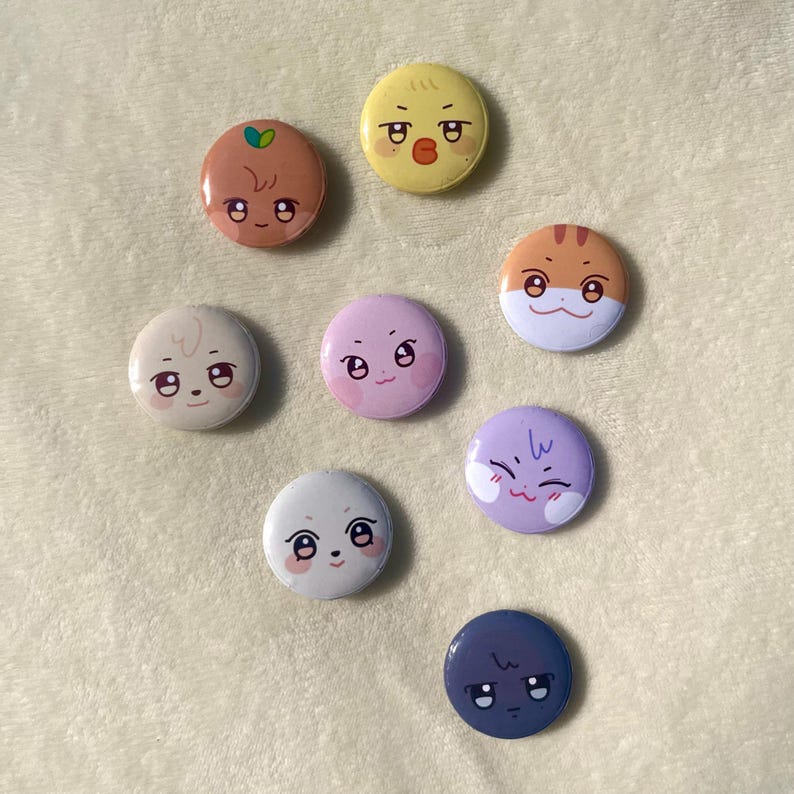 Puede incluir: Ocho botones redondos de colores con diferentes caras de dibujos animados. Los botones est&aacute;n sobre una superficie blanca y peluda.