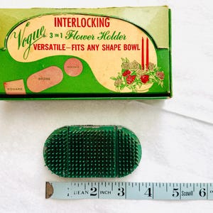 May include: Vintage Vogue 3-in-1 flower holder with a green box. The box reads "INTERLOCKING 3 in 1 Flower Holder VERSATILE - FITS ANY SHAPE BOWL". A green flower frog is next to a measuring tape. The flower frog is approximately 3 inches long.