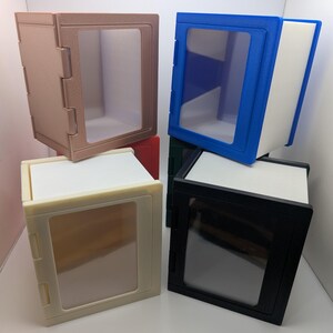 May include: A collection of five stackable storage boxes with clear front panels. The boxes are available in beige, blue, black, red, and dark green. Each unit features a rectangular frame with a transparent window, designed for organizing items.