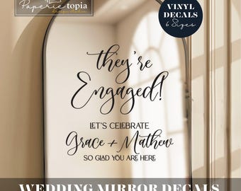 May include: A black arched mirror with the text "they're Engaged!" and "Let's Celebrate Grace + Mathew". The mirror also has the text "Wedding Mirror Decals" and "customized sizes". A logo for Paperie Topia is in the upper left.