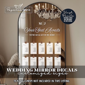 May include: A large arched mirror with a black frame, featuring a seating chart for a wedding. The mirror has the text "Your Seat Awaits" and "Wedding Mirror Decals". Individual seating cards are attached to the mirror. A chandelier hangs above.