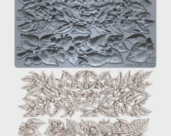 Puede incluir: Un molde de silicona gris con intrincados diseños botánicos en relieve de hojas, bayas y nueces. El molde incluye etiquetas de texto que indican capacidades de 52ml/78g, 36ml/54g y 7,4ml/11g, con la marca Hazel & Bay IOD impresa en la esquina.
