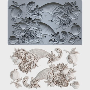 May include: A gray silicone mold sheet featuring embossed designs of two cornucopias filled with flowers, fruits, and leaves, alongside individual pomegranate motifs. The text "CORNUCOPIAS IOD" is visible, with specific volume and weight measurements in ml and g.