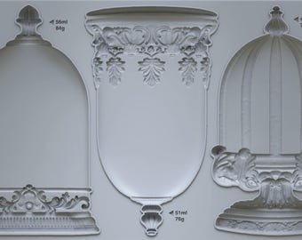 Puede incluir: Un molde de silicona gris claro con tres diseños empotrados distintos etiquetados como LES CLOCHES IOD. El molde de la izquierda tiene forma de cúpula, el central es un elemento arquitectónico decorativo y el de la derecha es una jaula de pájaros.