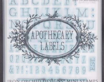 Puede incluir: Un juego de mini sellos Iron Orchid Designs en un estuche de plástico translúcido. El empaque presenta el texto Apothecary Labels dentro de un marco floral ovalado, con una cuadrícula de letras, números y signos de puntuación debajo.
