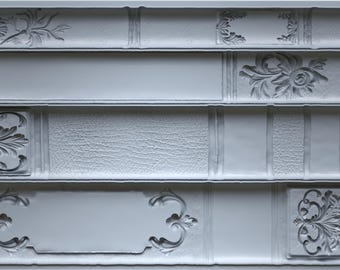 Puede incluir: Un molde de silicona gris con forma rectangular, con cuatro secciones diseñadas para parecerse a lomos de libros. Cada sección tiene detalles decorativos florales y de volutas, con el texto "BOOKISH IOD" y medidas de volumen.