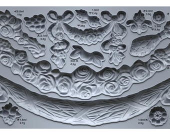 Puede incluir: Un molde de silicona gris rectangular que presenta varios diseños florales y decorativos de guirnaldas. El molde incluye múltiples cavidades para el vaciado, con medidas específicas de volumen y peso impresas junto a cada forma. El texto SWAGS IOD es visible.