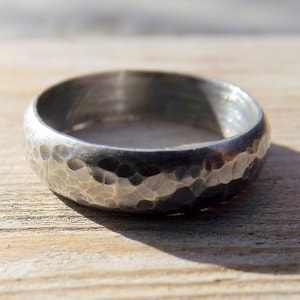 May include: A silver ring with a hammered texture. The ring is wide and has a rounded profile.