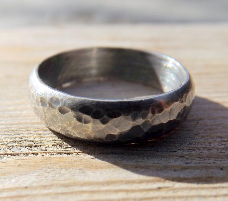 May include: A silver ring with a hammered texture. The ring is wide and has a rounded profile.