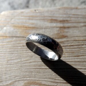 May include: A silver hammered band ring with a smooth interior. The ring is on a wooden surface.