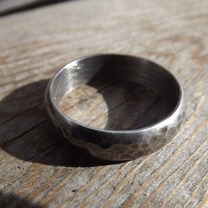 May include: A silver ring with a hammered texture. The ring is thick and has a rounded profile.