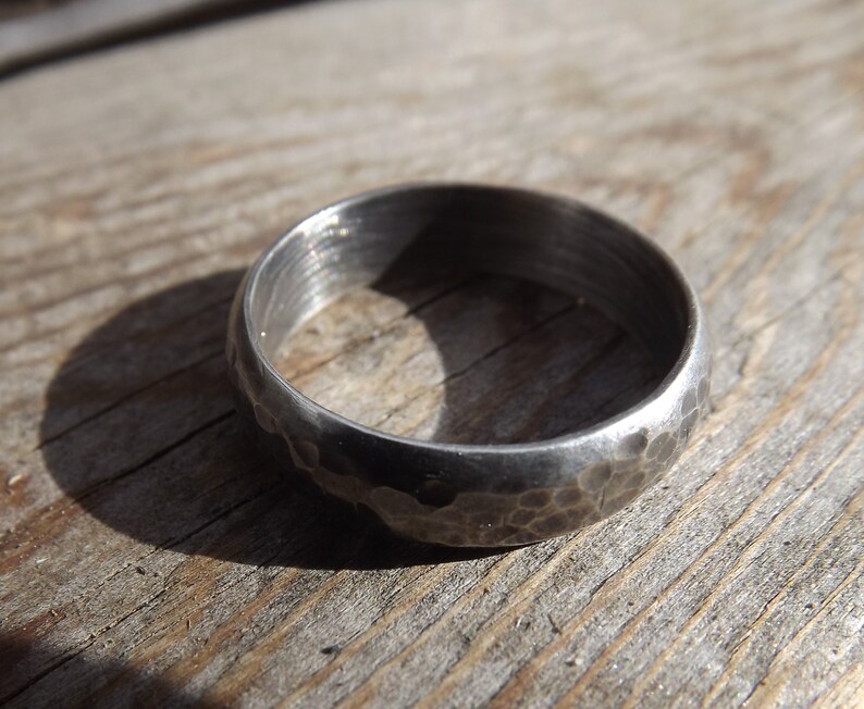 May include: A silver ring with a hammered texture. The ring is thick and has a rounded profile.
