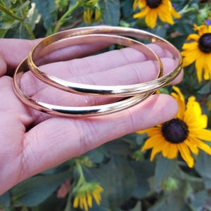 May include: Two gold bangle bracelets stacked on top of each other. The bracelets are smooth and shiny.