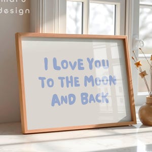 May include: A rectangular wooden frame containing a white print with the light blue text I LOVE YOU TO THE MOON AND BACK. The text is written in a rounded, sans-serif font. The brand name maru design is printed in the top left corner.