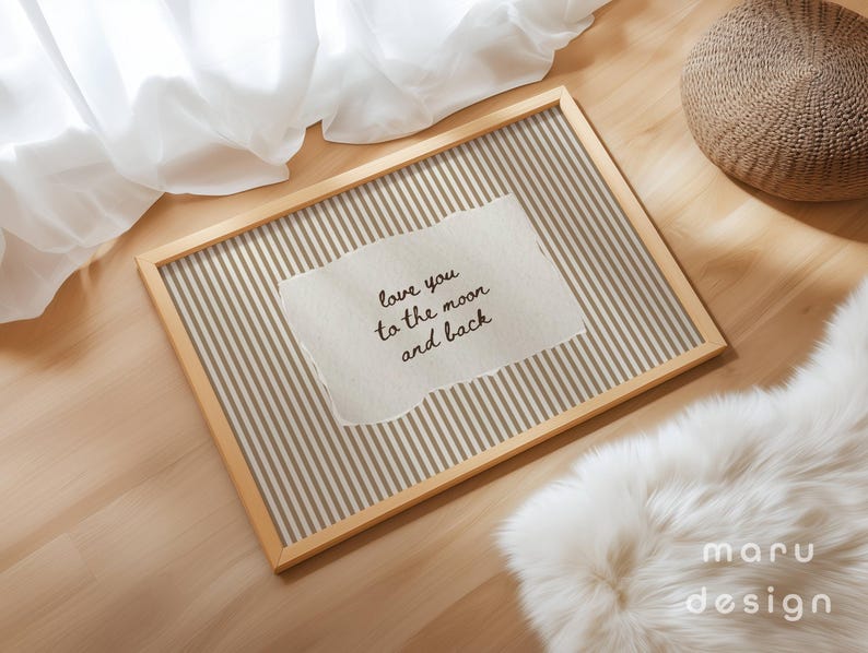 May include: A rectangular wooden frame with a striped background and a torn paper insert. The paper reads "love you to the moon and back" in black script. The frame is on a wooden surface with a white fur rug and a woven pouf.