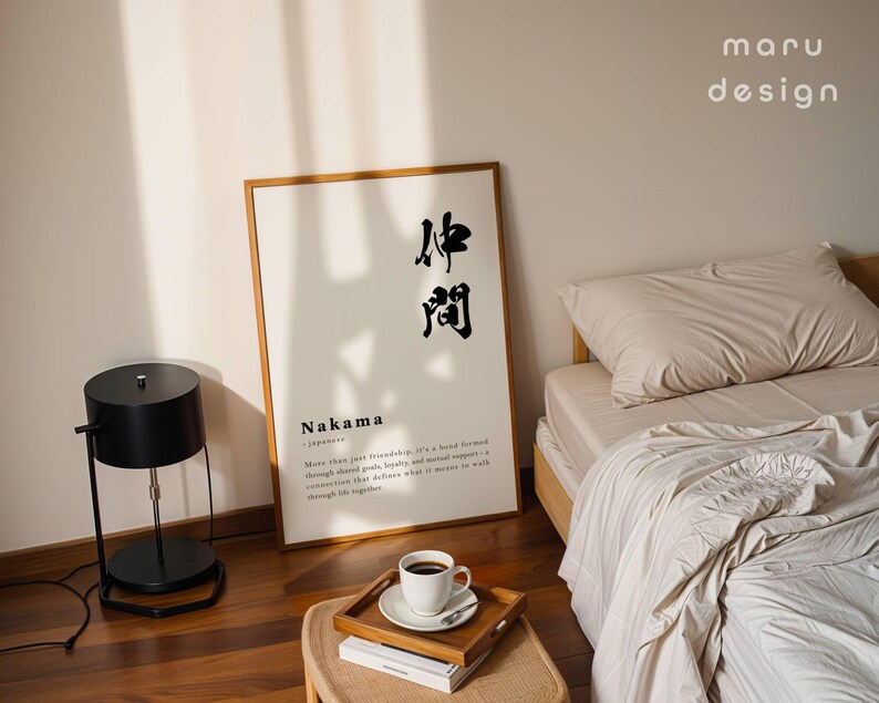 May include: A rectangular wall art print in a wooden frame featuring the Japanese kanji for Nakama, the word Nakama, and a definition text. The print is displayed on a floor next to a black lamp and a bed with beige bedding and a wooden tray with a cup.
