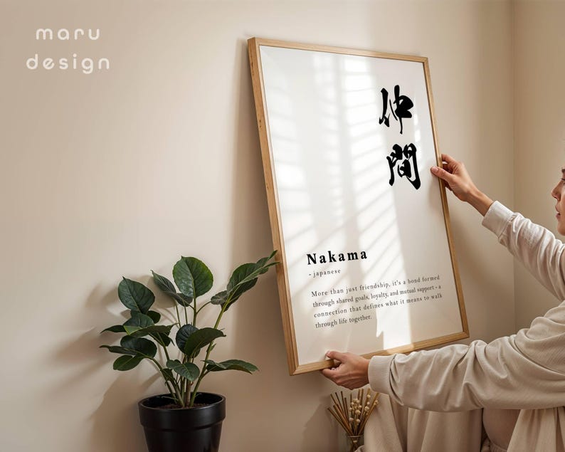 May include: A rectangular wall art print in a light wood frame featuring the Japanese kanji for Nakama, the word Nakama, and a definition text describing a bond formed through shared goals, loyalty, and mutual support. The text maru design is visible.