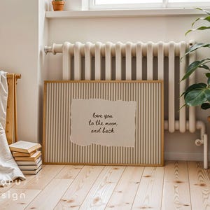 May include: A framed print with a vertical striped background and a torn paper insert. The insert features the text "love you to the moon and back" in a handwritten style. The frame is light brown, and the print is displayed indoors.